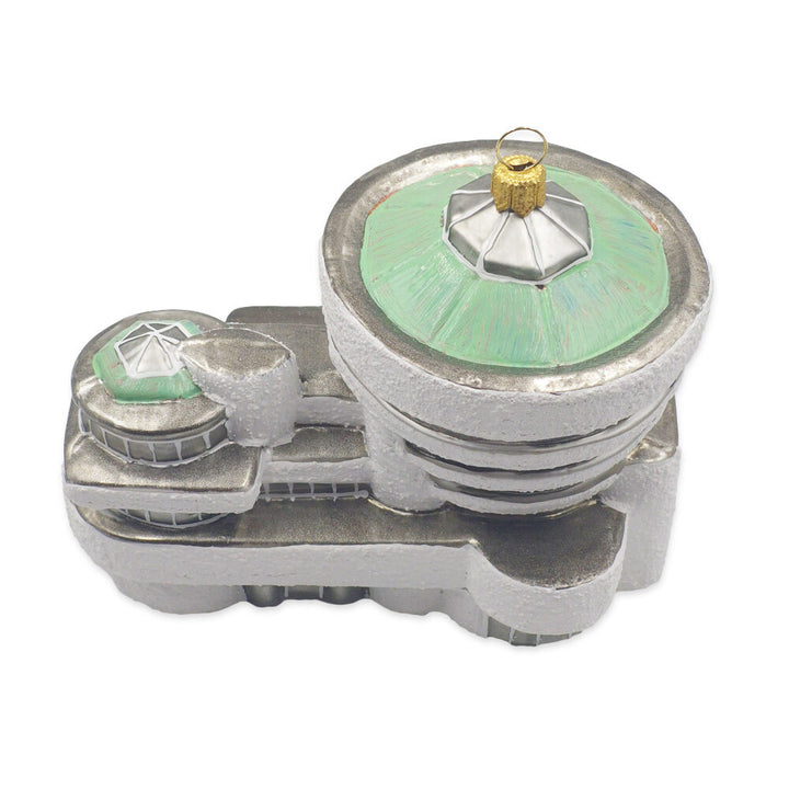 The Guggenheim Building Ornament is a silver and green decoration shaped like a futuristic building, featuring circular and rectangular elements inspired by the Guggenheim Museum, with a loop on top for hanging.