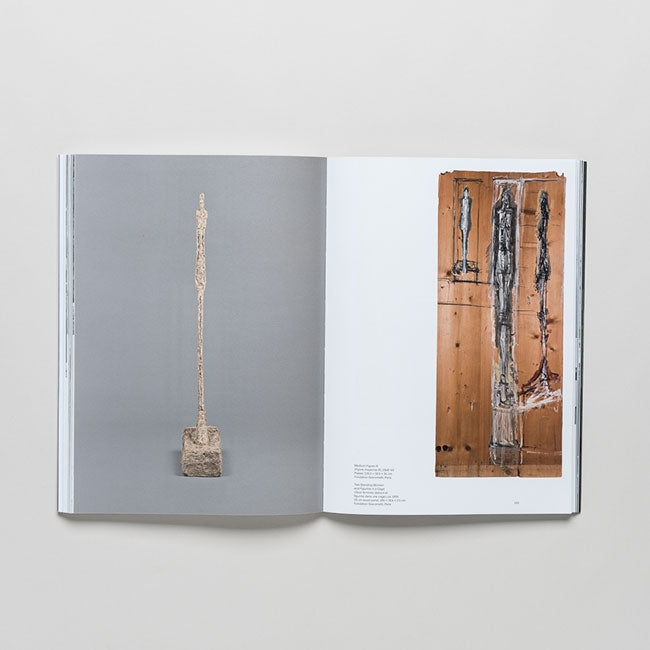 The open book "Giacometti" displays on the left a photo of an Alberto Giacometti figurative sculpture, and on the right an abstract painting with vertical shapes on brown—both featuring his signature elongated forms.