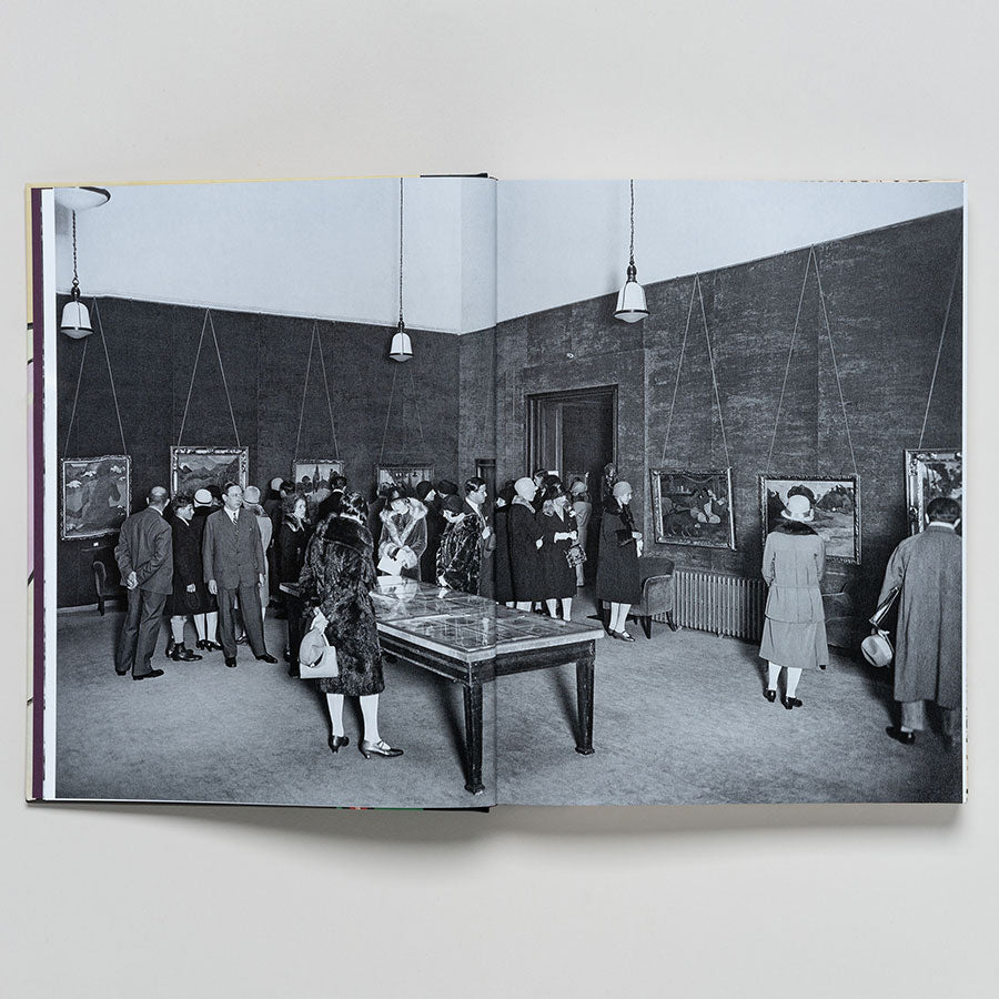 A black-and-white photo from the Thannhauser Collection: French Modernism at the Guggenheim shows people in formal attire mingling and viewing modern art in a gallery with high ceilings and pendant lights, evoking the museum’s iconic ambiance.