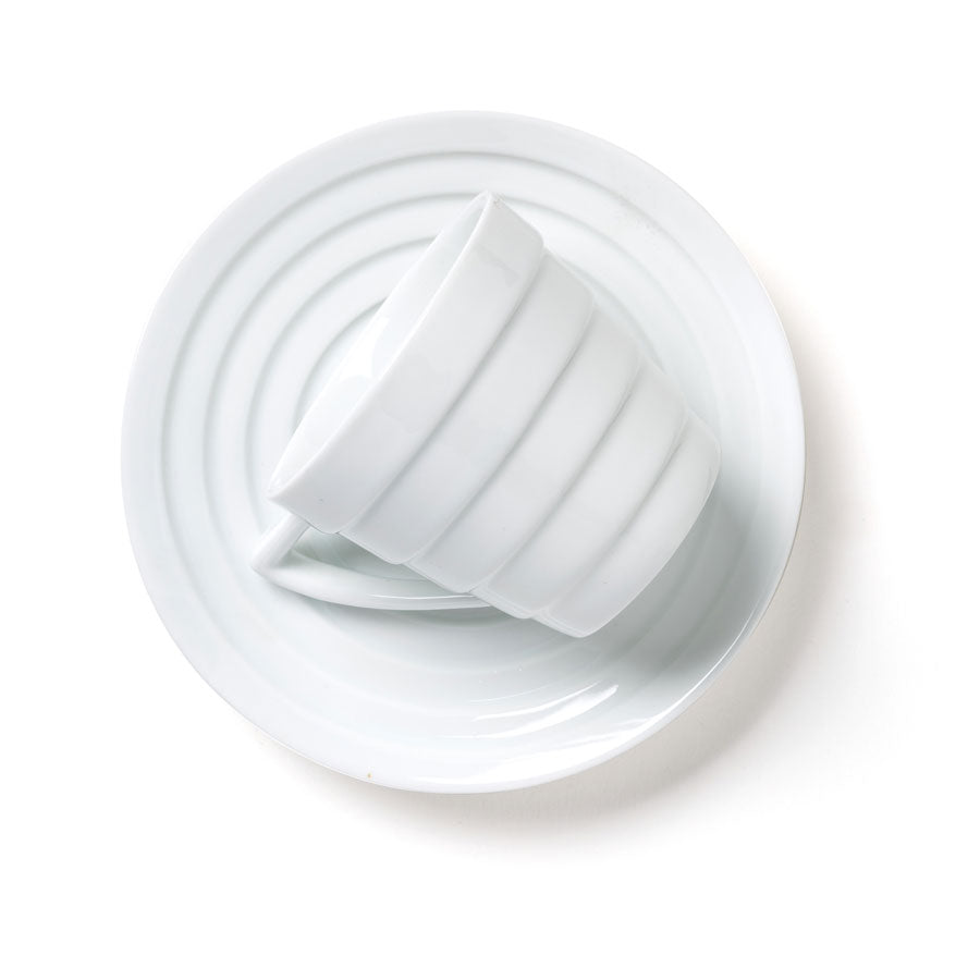 The Guggenheim Spiral Espresso Cup Set features a white ceramic cup angled in a matching saucer with circular ridged patterns, all displayed against a plain white background.