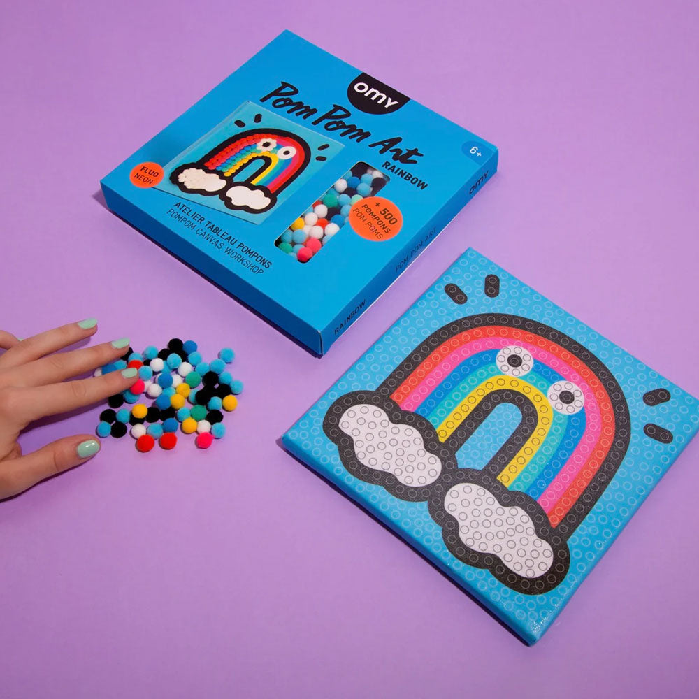 A hand holds colorful pom poms from the Guggenheim Museum Rainbow Pom Pom Art kit to build fine motor skills.
