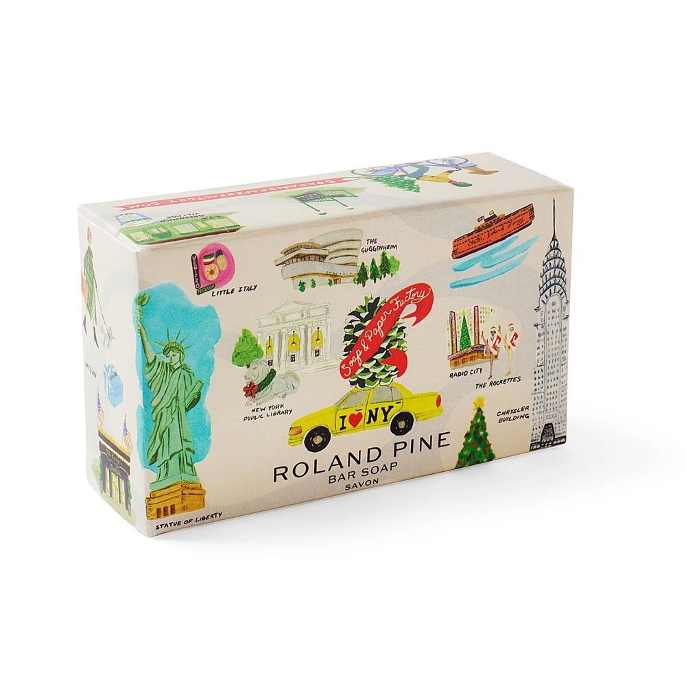 The Holiday in New York Roland Pine 5 oz Boxed Shea Butter Soap Bar features vibrant illustrations of NYC landmarks like the Statue of Liberty, Chrysler Building, yellow taxi, and city scenes on its packaging.