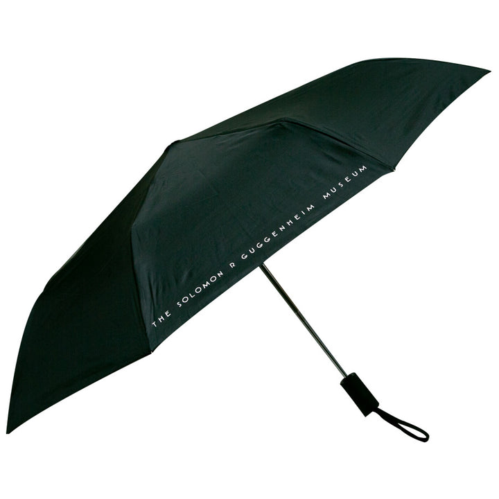 The Guggenheim Skylight Umbrella is a sleek black umbrella with "THE SOLOMON R GUGGENHEIM MUSEUM" in white on the edge. It features automatic open and close, plus a black handle with wrist strap—an ideal gift for any art lover.