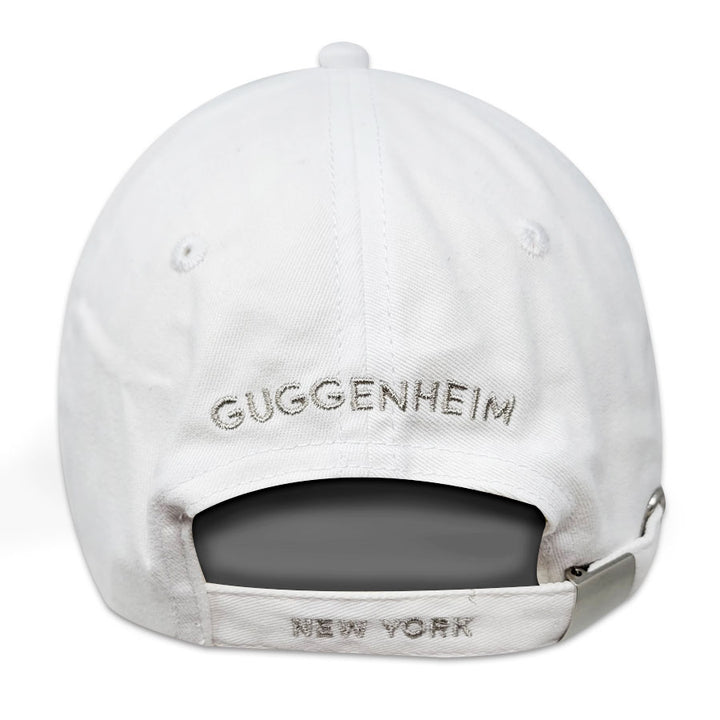 The Guggenheim "G" White Cap is a cotton adjustable baseball cap, seen from the back, with "GUGGENHEIM" embroidered above the strap and "NEW YORK" stitched on the adjustable strap.