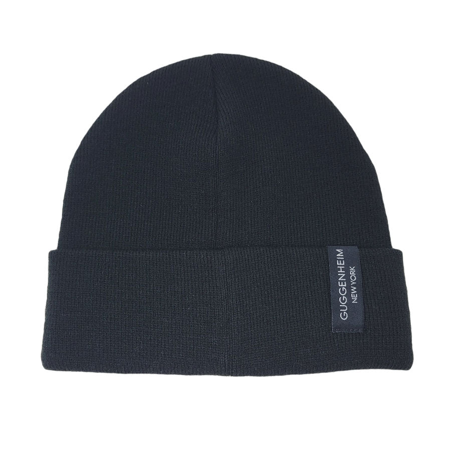 The Guggenheim Black Beanie is a classic, plain black knit with a folded brim and a small rectangular "GUGGENHEIM NEW YORK" label—an essential winter accessory.