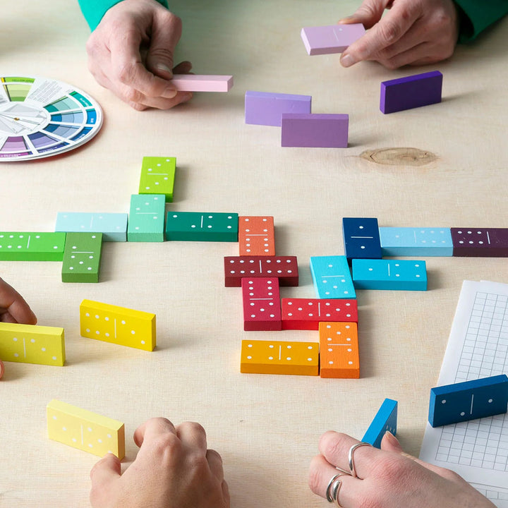 Four enjoy Gradient Dominoes by Guggenheim Museum—a vibrant family game with wooden dominoes, color wheel, and notepad.