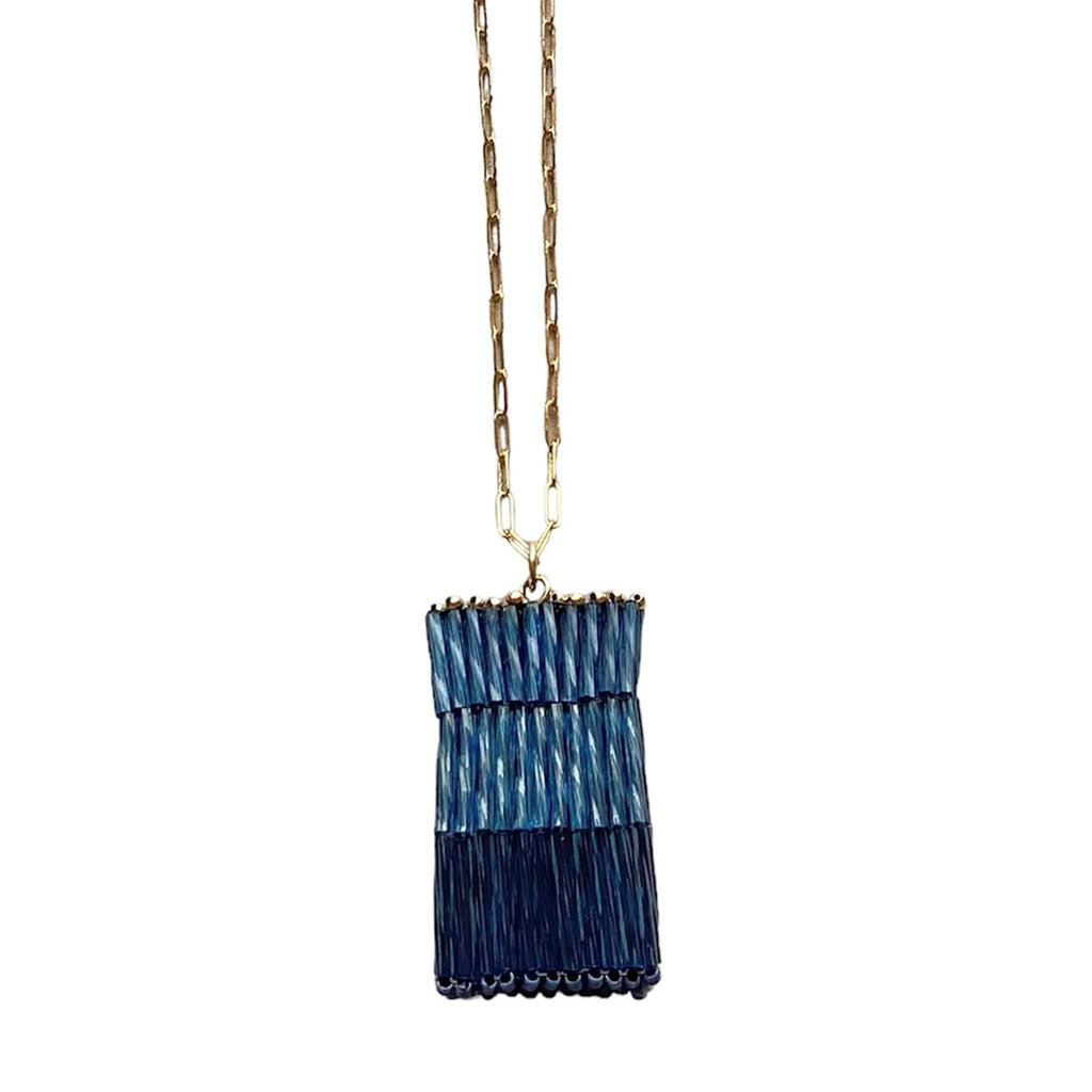 The Trecy Bleich Rice Stack Necklace Denim features a gold chain and a rectangular pendant with layered blue and navy textures for a chic, two-toned fringe look—ideal as a statement piece or paired with your favorite bangle.