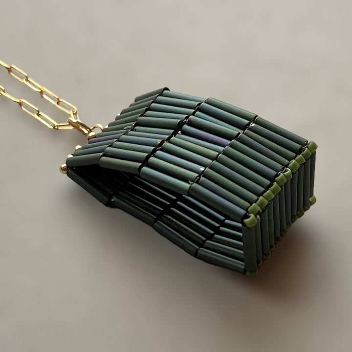 The Trecy Bleich Rice Stack Necklace Moss features a gold chain with dark green cylindrical beads in a woven, geometric design, highlighting chunky, modern handcrafted style from the Rice collection against a neutral background.