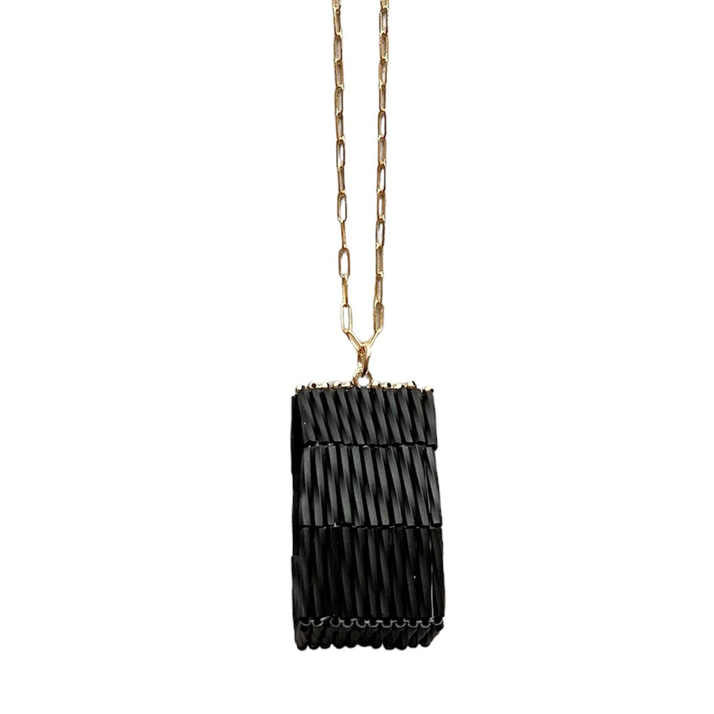 The Trecy Bleich Rice Stack Necklace Charcoal features a gold chain and a handcrafted rectangular black pendant with a pleated design. Part of our Rice collection, it hangs vertically for a unique, modern look.