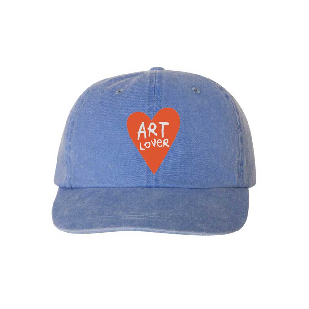 The Art Lover Youth Cap, designed by Humberto Cruz, features blue fabric, a red heart, and playful “ART LOVER” lettering—perfect for kids who love art and need stylish sun protection.