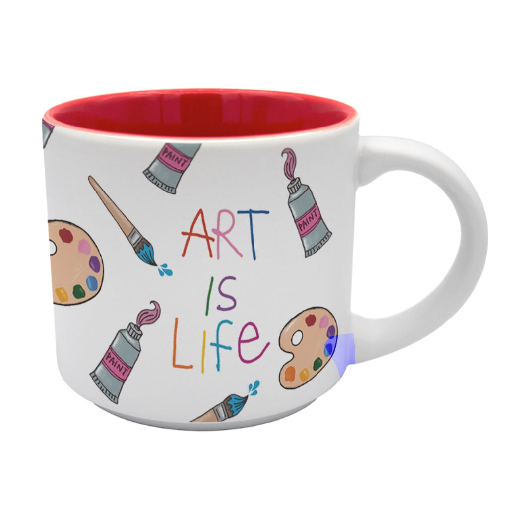 The Art is Life Mug is a white ceramic mug with a red interior, decorated with colorful paintbrushes, paint tubes, palettes, and "ART IS LIFE" in rainbow letters—an ideal addition to any artistic coffee mug collection.