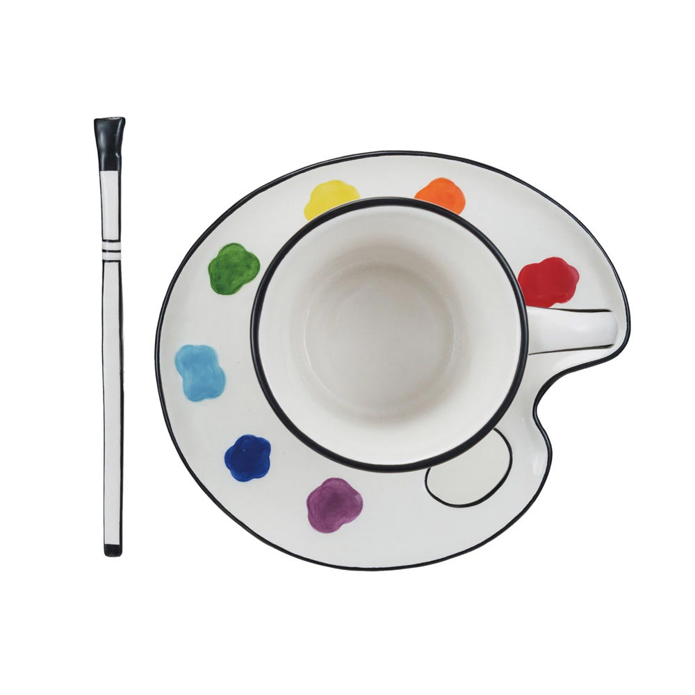 The Ceramic Paint Palette Saucer w/ Teacup & Brush Shaped Stirrer Set of 3 includes a palette-inspired cup and saucer with colorful paint accents and a paintbrush-shaped stirrer, all displayed on a white background.