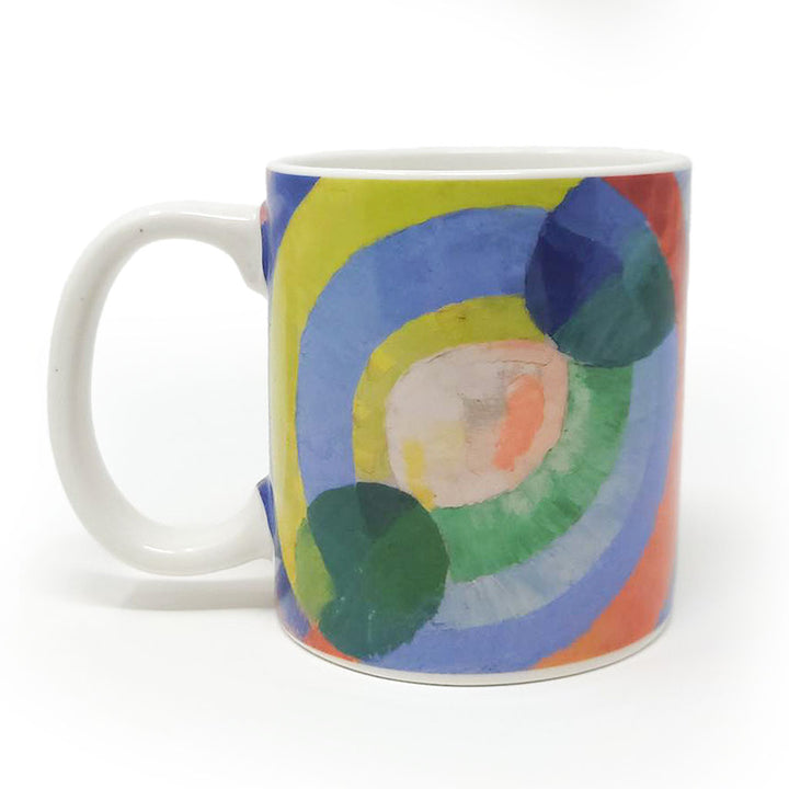 The Delaunay, Circular Forms Mug is a white ceramic art mug featuring a colorful design inspired by Robert Delaunay, with overlapping green and blue circular forms and concentric circles in blue, yellow, green, and orange.