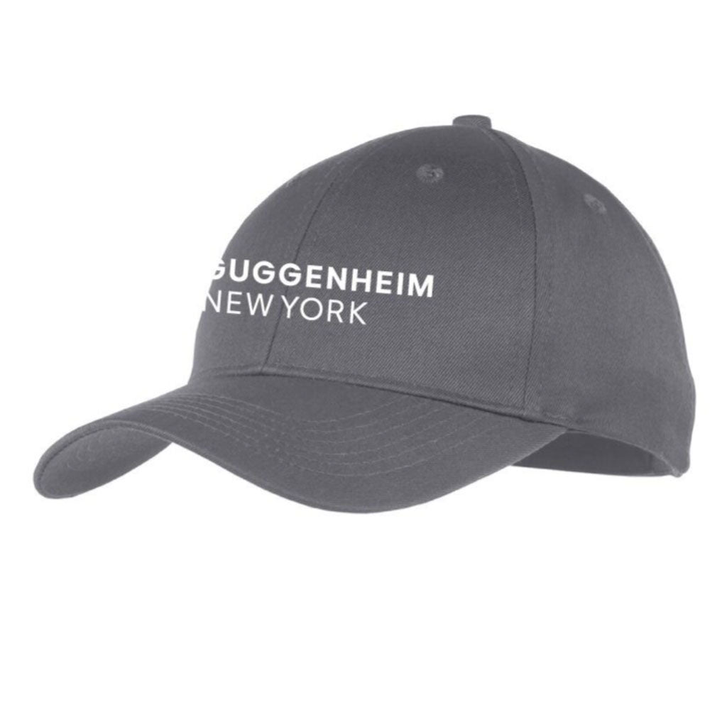 The Guggenheim Youth Cap is a dark gray, adjustable kids’ cap featuring white "GUGGENHEIM NEW YORK" text on the front, a curved brim, and visible stitching for a classic style.