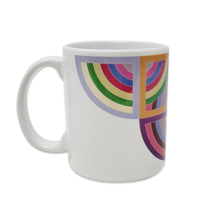The Stella, Harran II Mug is a stylish coffee mug with a handle, featuring a colorful geometric semi-circle pattern in green, red, purple, blue, and gold on one side against a crisp white background.