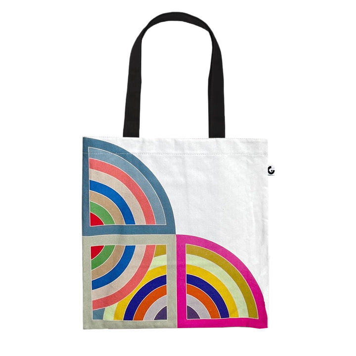 The Stella, Harran II Tote is a white cotton bag with black handles, showcasing vibrant semi-circular geometric patterns in blue, green, red, yellow, pink, and gray on the lower corners—a standout statement piece.