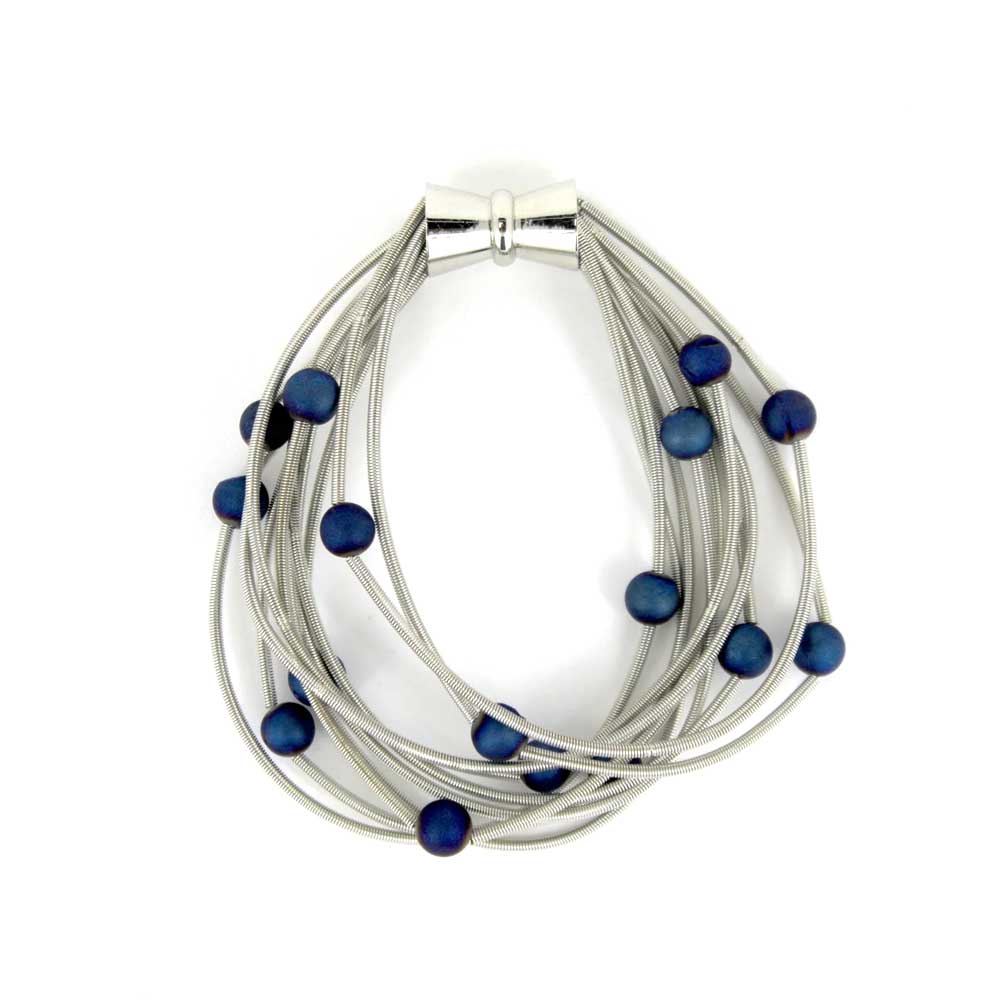 The Blue Geode Piano Wire Bracelet features multiple strands of silver steel wire with a magnetic clasp and small, round dark blue beads spaced throughout.
