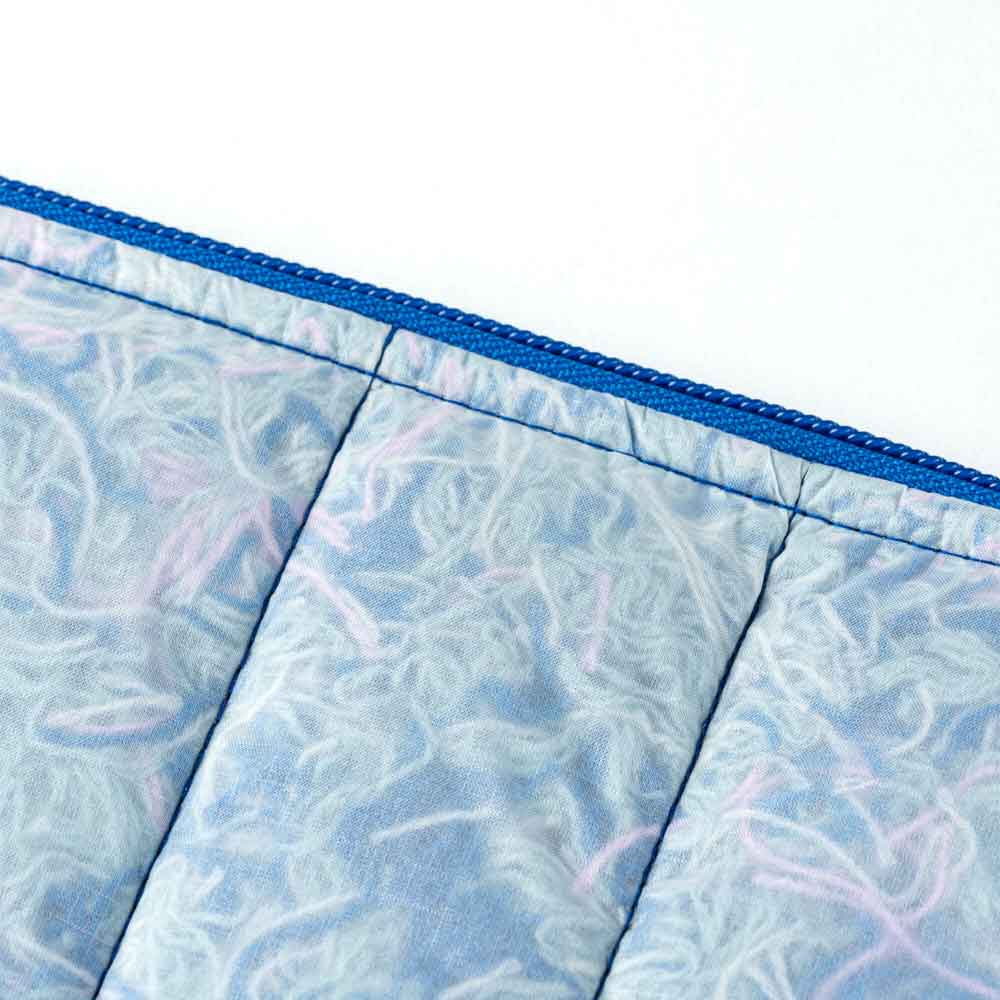 Close-up of the Scrap Stuffed Pouch, a blue VERLOOP zipper pouch crafted from eco-friendly quilted fabric with a blue zipper and soft, wavy white and light purple patterns inspired by scrap yarn.