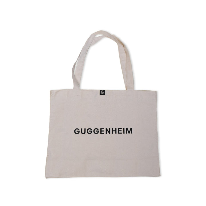The Guggenheim Constellation Tote Bag New York, Natural, is an organic cotton tote with two handles and bold black GUGGENHEIM lettering on the front—a classic museum bag perfect for daily use.