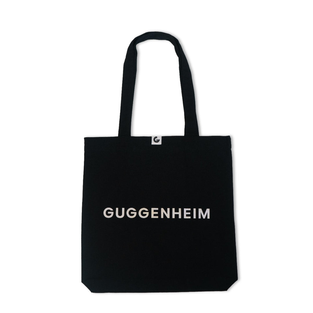 The Guggenheim Constellation Tote Bag New York, Black, features "GUGGENHEIM" in bold white letters across the front, two handles, and a small white tag at the top center.