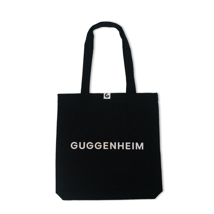 The Guggenheim Constellation Tote Bag New York, Black, features "GUGGENHEIM" in bold white letters across the front, two handles, and a small white tag at the top center.