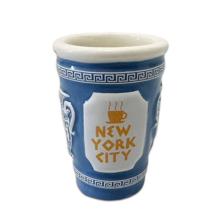The 3D NYC Coffee Cup Shot Glass is a ceramic, 2 oz shot glass styled after a Greek diner cup with a blue and white pattern. It features "NEW YORK CITY" and a steaming coffee icon on the front. Hand wash only.