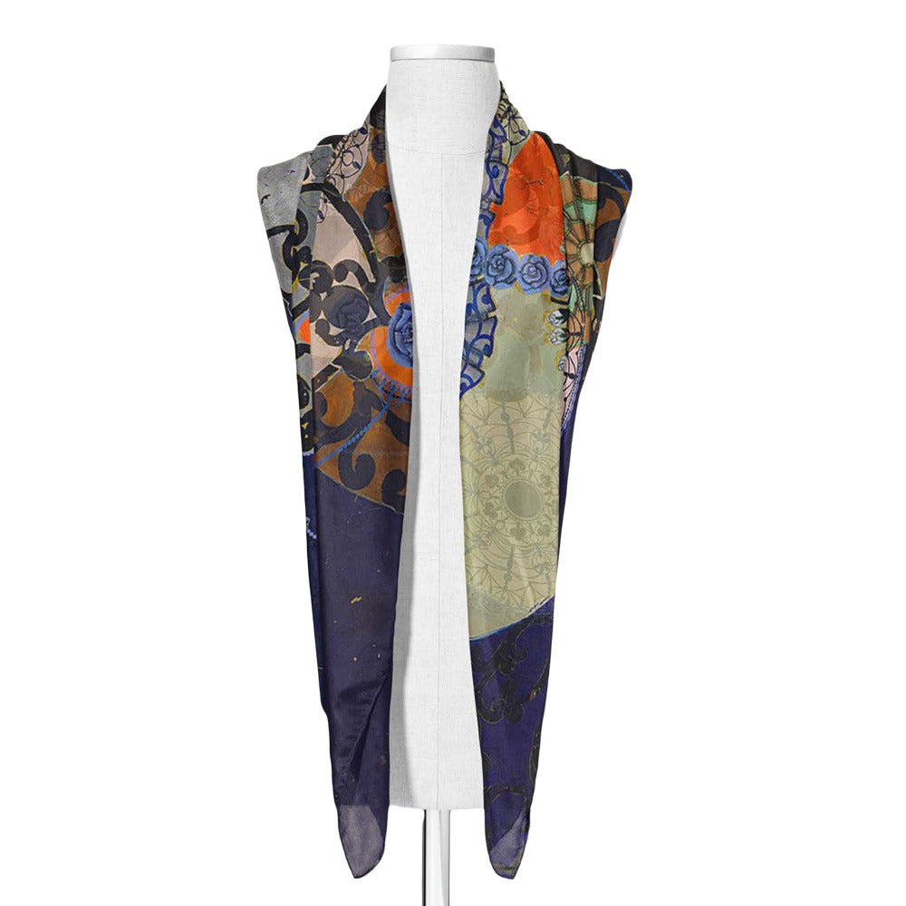 The Guggenheim Beatriz Milhazes Silk Scarf, In Albis, drapes over a white dress form, showcasing vibrant blue, orange, green, and brown abstract swirls, florals, and geometric patterns for a striking wearable art statement.