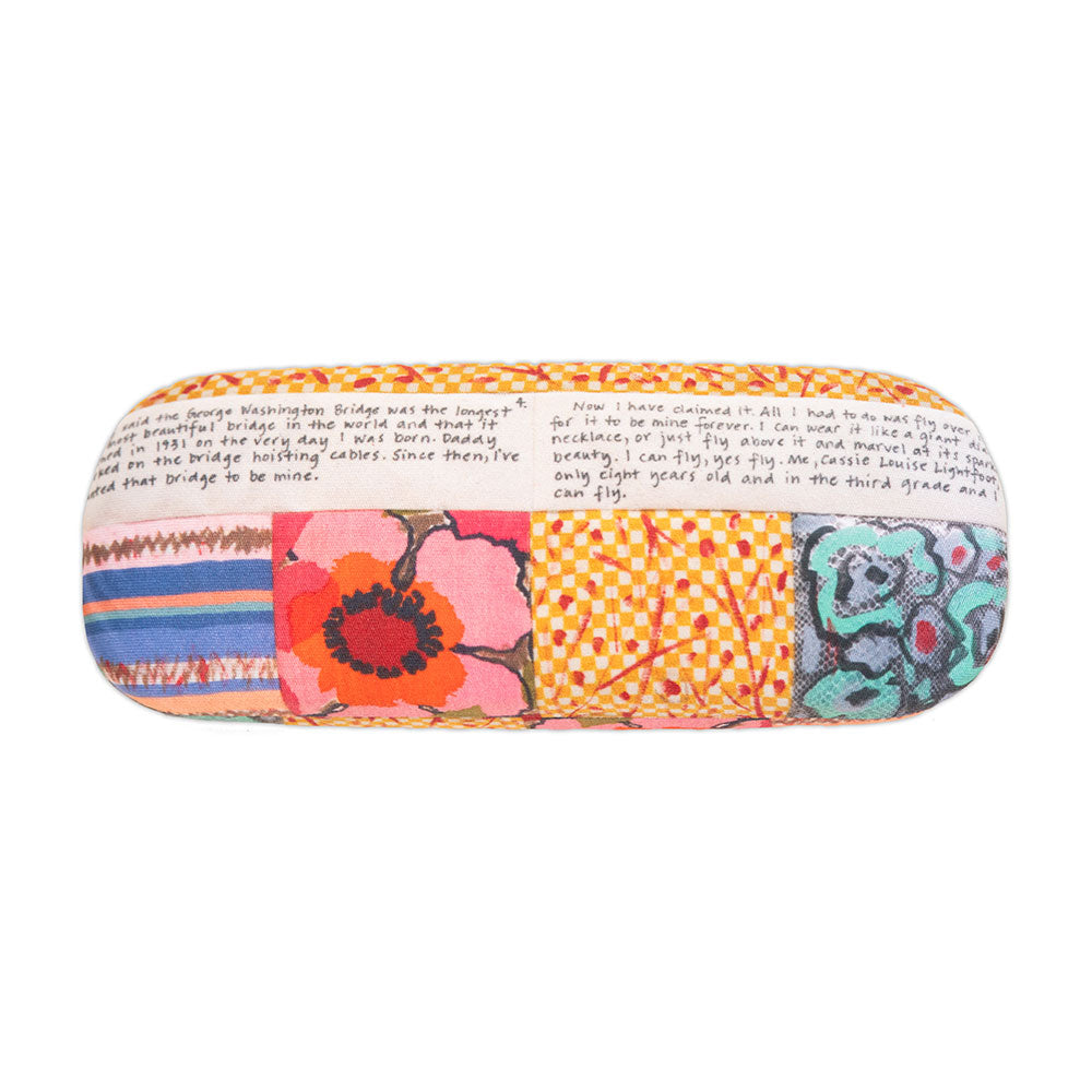 The Faith Ringgold Tar Beach Eyeglass Case features a vibrant patchwork of florals, stripes, checks, and handwritten text at the top. Includes a soft microfiber cloth for easy lens cleaning.