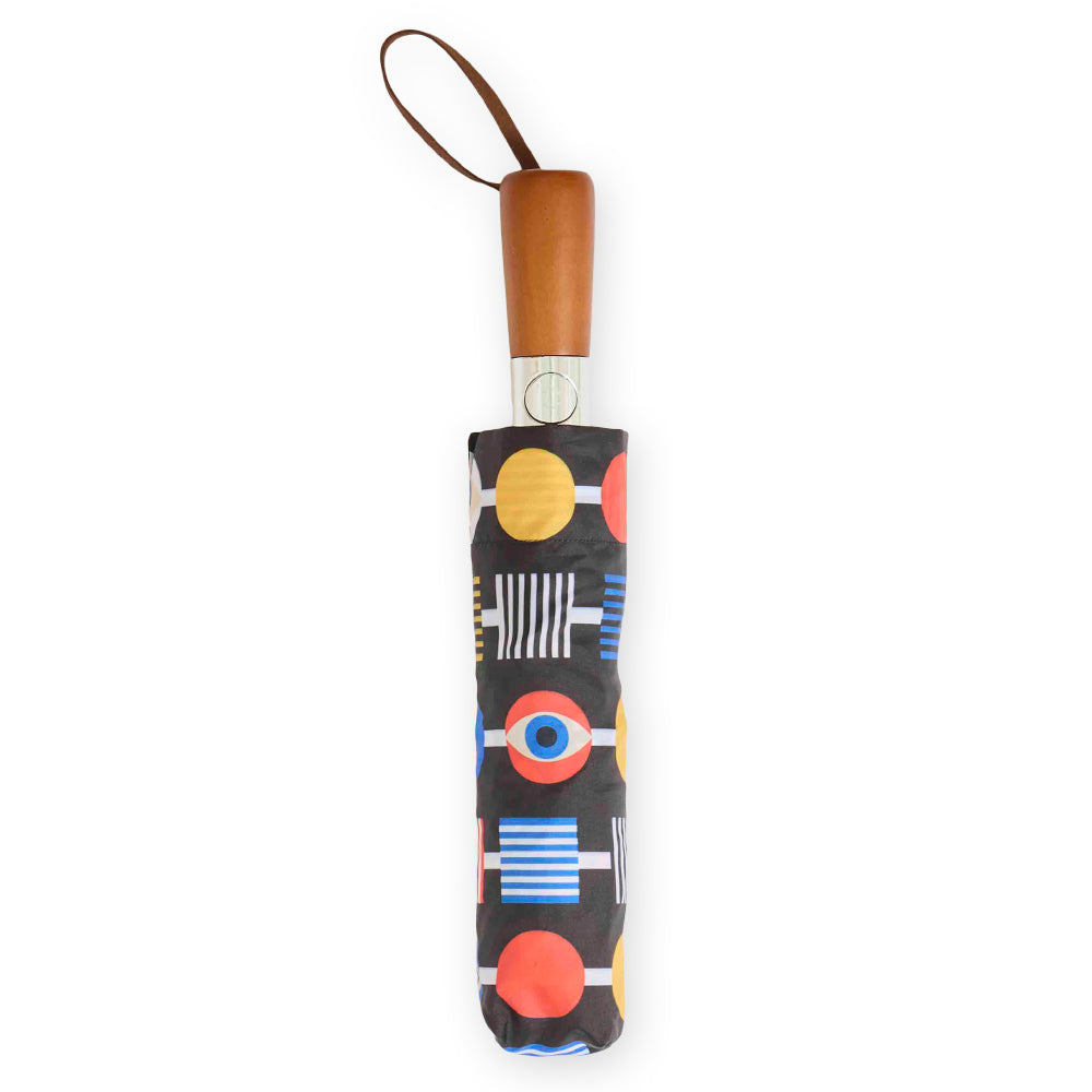 The Eye Collection Travel Umbrella by Guggenheim Museum features a wooden handle and a bold geometric multicolor cover.