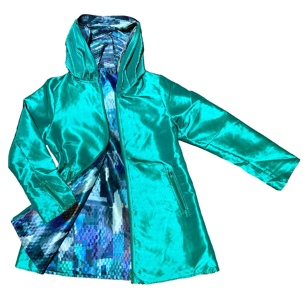 The Delaunay Window Reversible Jacket is a shiny turquoise women's zip-front jacket with a high collar, side pockets, and a colorful geometric blue, purple, and teal lining shown when worn open.