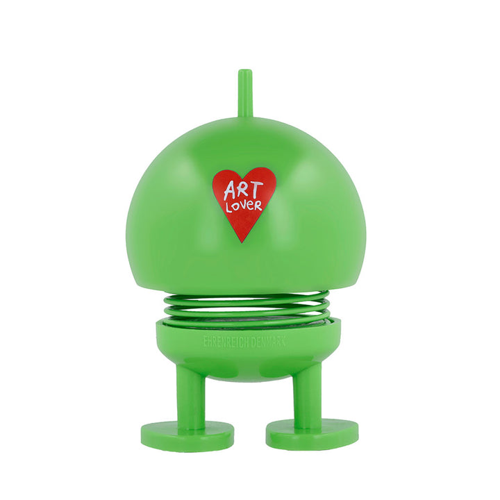 The Hoptimist x Humberto Cruz Art Lover, Green Figure is a playful, round, green figurine with spring legs, feet, a top stem, and features a red heart labeled ART LOVER on its body. Inspired by Gustav Ehrenreich’s original design.