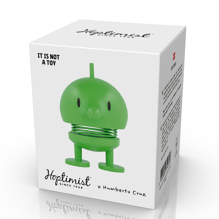 A white box shows the green, round Hoptimist x Humberto Cruz Art Lover figure with spring legs and a beak-like nose. Text reads “It is not a toy and Hoptimist x Humberto Cruz.” Product details appear on the sides.