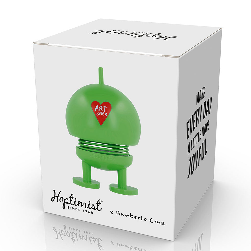 A white box displays the Hoptimist x Humberto Cruz Art Lover, a green figure with "Art Lover" in a red heart. The box says: Make every day a little more joyful and Hoptimist x Humberto Cruz. Designed by Gustav Ehrenreich.
