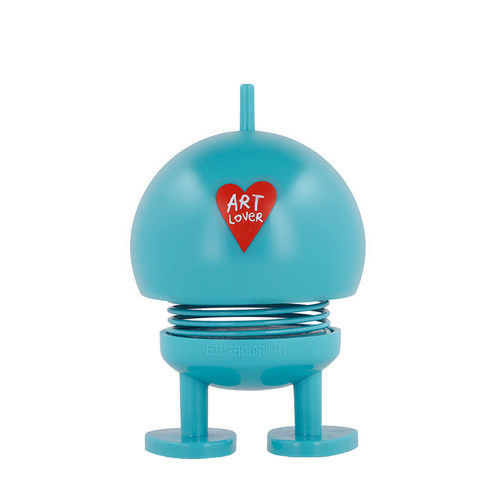 The Hoptimist x Humberto Cruz Art Lover, Blue Figure is a round, blue figurine with a spring body, flat feet, and a front red heart labeled "ART LOVER"—a special collaboration design by Humberto Cruz.