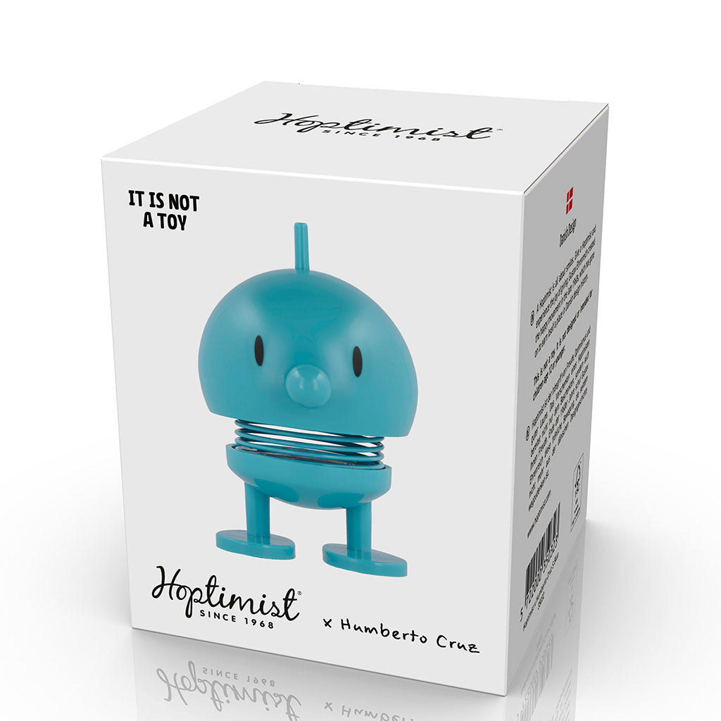 The box features the Hoptimist x Humberto Cruz Art Lover Blue Figure, a round spring-based positive figurine with legs and a small beak. The box reads "It is not a toy," shows the Hoptimist logo, and highlights the collaboration.