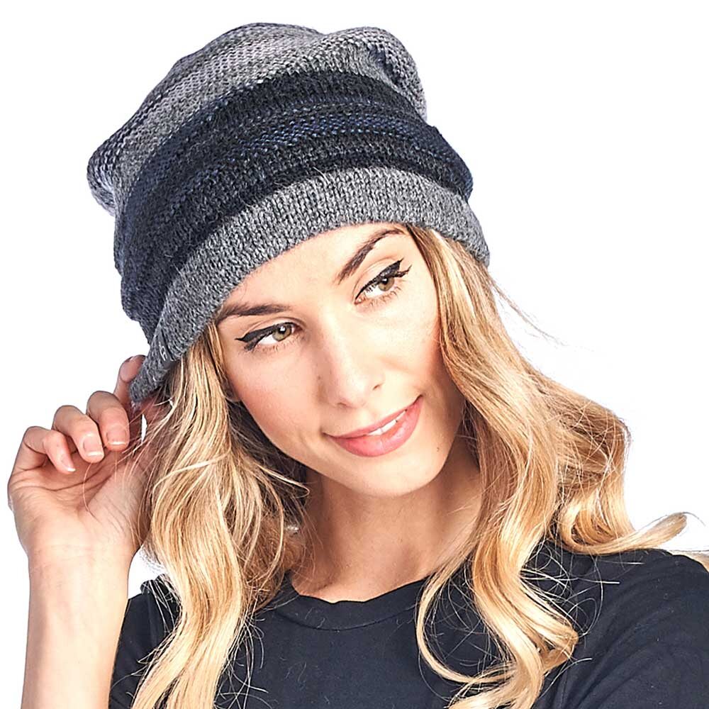 A woman with long blonde hair smiles slightly and looks to the side, touching the edge of her Colorado Alpaca Beanie in charcoal, a soft baby alpaca knit hat with gray and black stripes.
