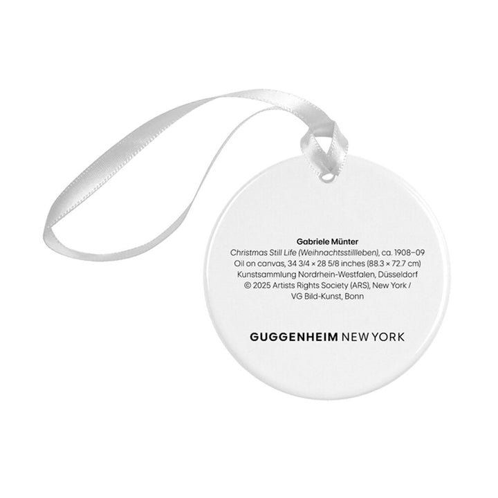 The Gabriele Münter, Christmas Still Life Ornament is a round porcelain ornament with a white ribbon, featuring printed text about the artwork, museum credits, and the Guggenheim New York logo at the bottom.
