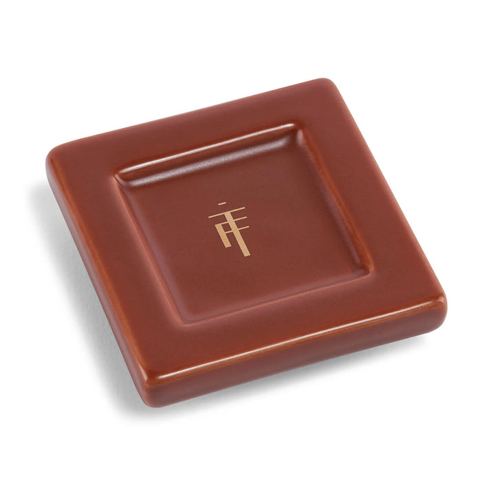 A square brown chocolate with a gold geometric logo from the Guggenheim Frank Lloyd Wright Tea Forte Gift Set.