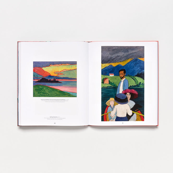 An open hardcover art book, "Gabriele Münter: Contours of a World," displays two colorful paintings—one of a sunset lake landscape and another featuring figures outdoors with mountains and a house in the background from the 2025 collection.