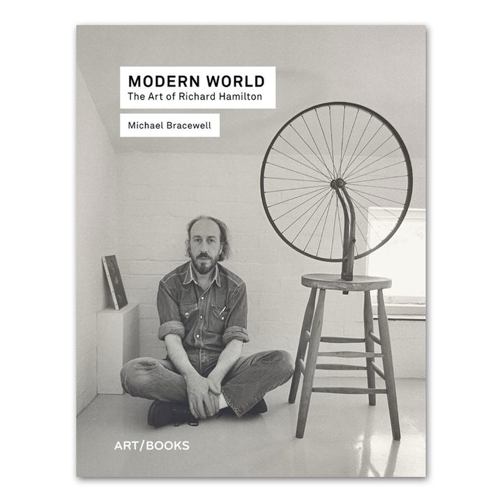 A man sits cross-legged by a Pop art chair with a bicycle wheel on the cover of Guggenheim’s *Modern World: The Art of Richard Hamilton*.
