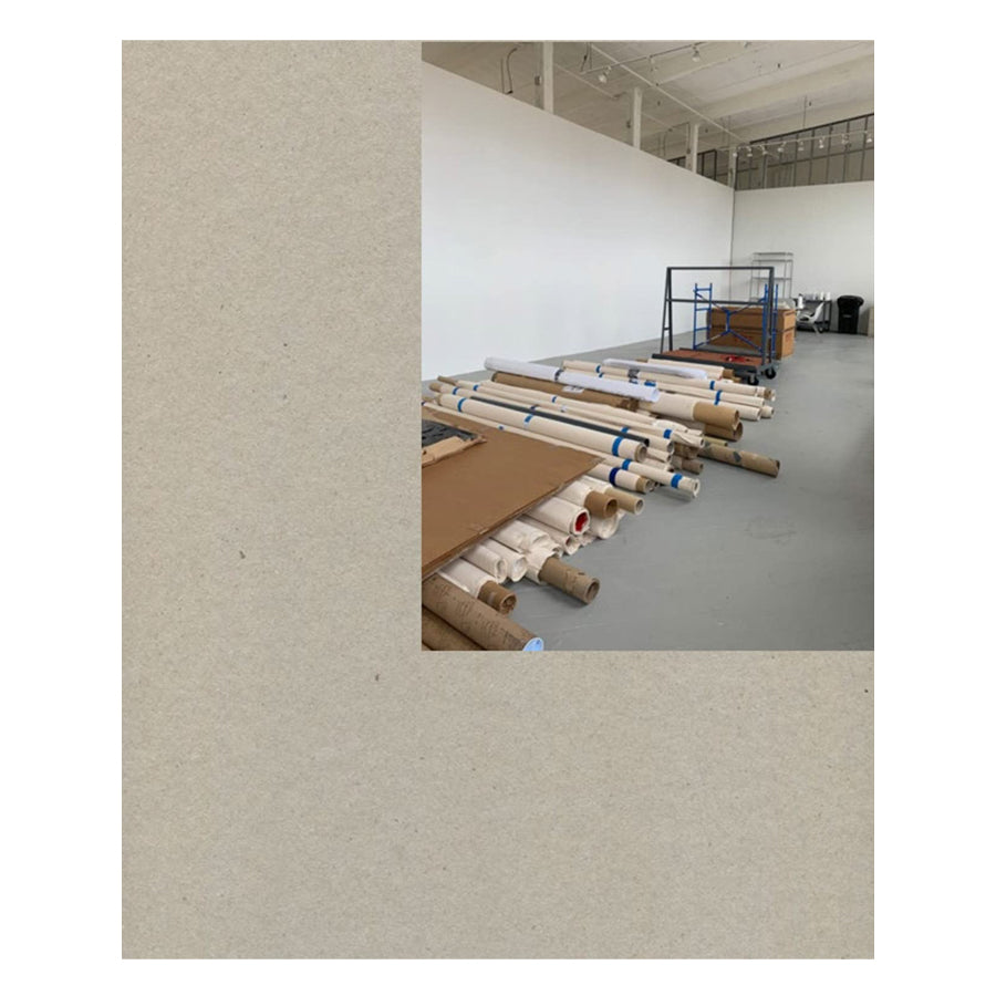 A photo of an industrial space with stacked brown paper rolls recalls the textured backgrounds of Glenn Ligon: Work, Work, Work, Work, Work, Work. A table and shelving add to the raw atmosphere.