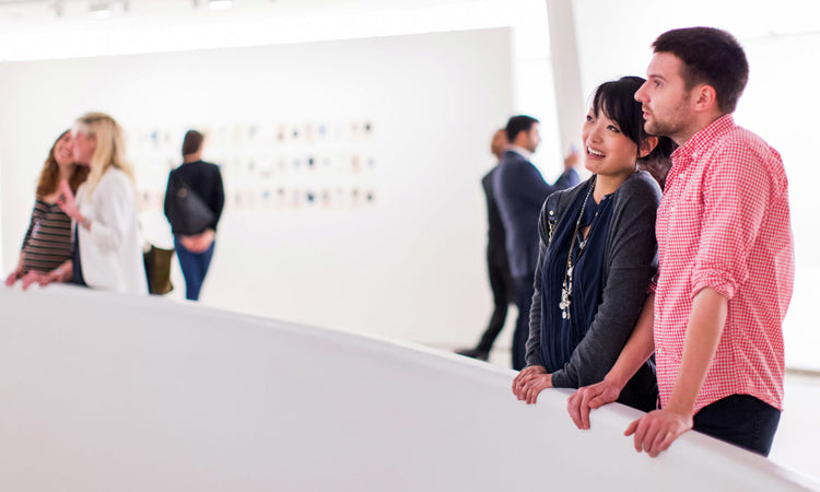 A couple stands together, looking at art in a bright, modern gallery with other visitors in the background.