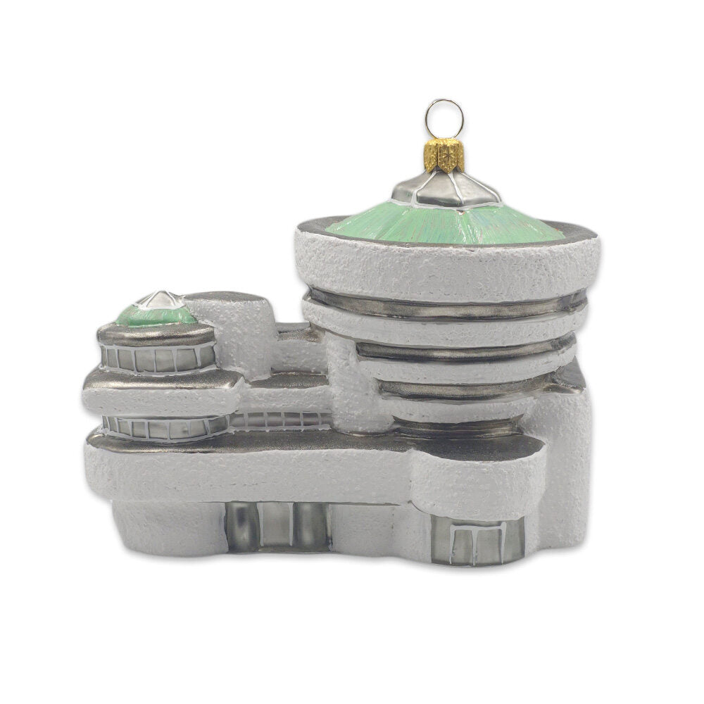 The Guggenheim Building Ornament is a glass decoration inspired by Frank Lloyd Wright’s design, featuring rounded edges, green-tinted domes, and a gold loop at the top for hanging.