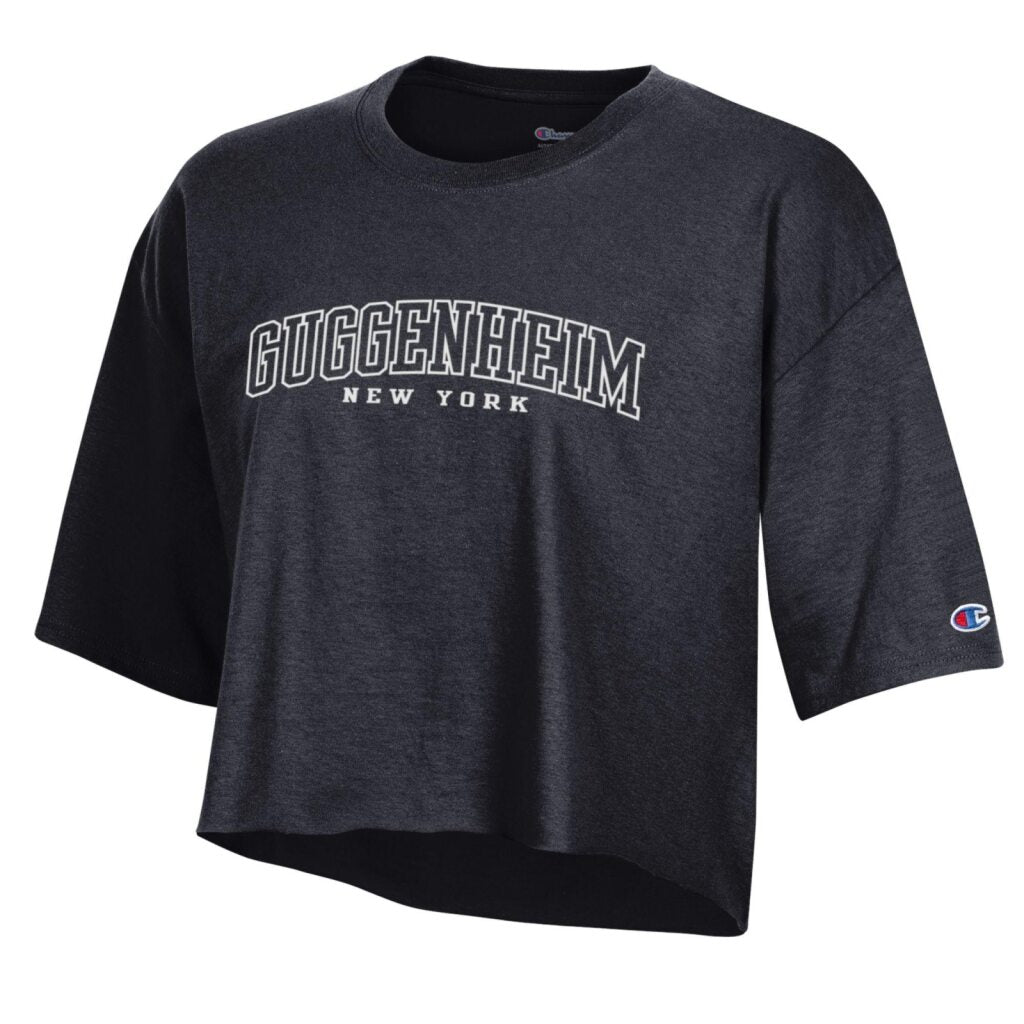 The Guggenheim Women's Boxy Crop T-Shirt is a black, 100% cotton top with “Guggenheim” in bold white letters above “New York,” and a Champion logo on the left sleeve.