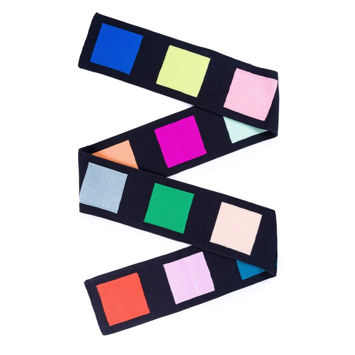 The Swatch Skinny Scarf is a dark, zigzag long winter scarf featuring large, evenly spaced color blocks—blue, yellow, pink, orange, magenta, green, red, and light blue—crafted from soft acrylic and machine washable for easy care.