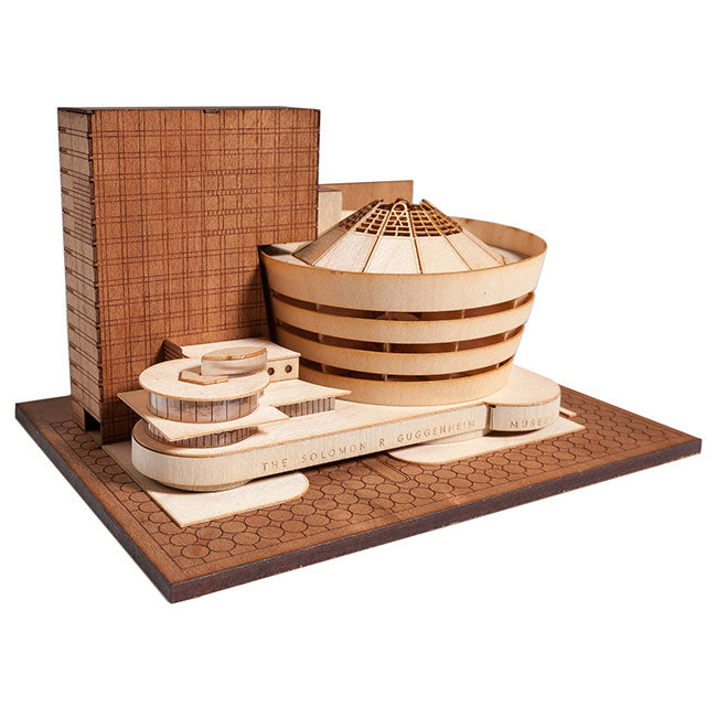 The Guggenheim Architectural Model Kit is a wooden replica of the iconic New York City museum, showcasing its signature circular design, spiral ramp, and adjacent rectangular structure on a detailed base.