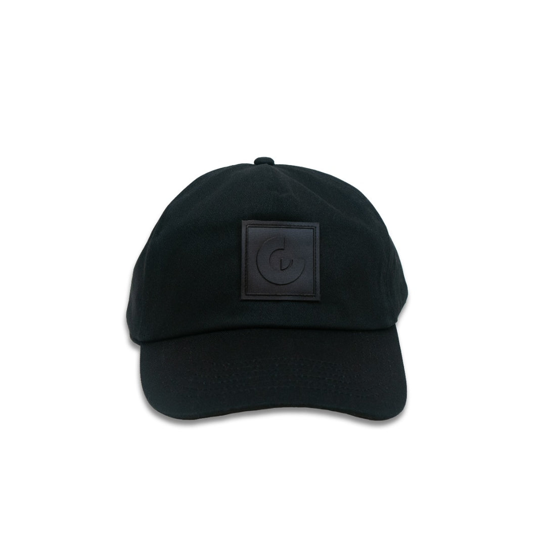 The Guggenheim Constellation Cap New York is a minimalist black cotton cap with an adjustable fit and a square embossed patch featuring a stylized G on the front, shown against a plain white background.