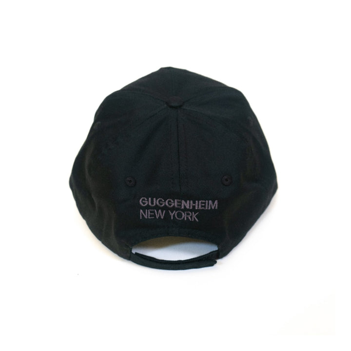 A minimalist black Guggenheim Constellation Cap New York viewed from the back, featuring light gray embroidered "GUGGENHEIM NEW YORK" above an adjustable cotton strap.