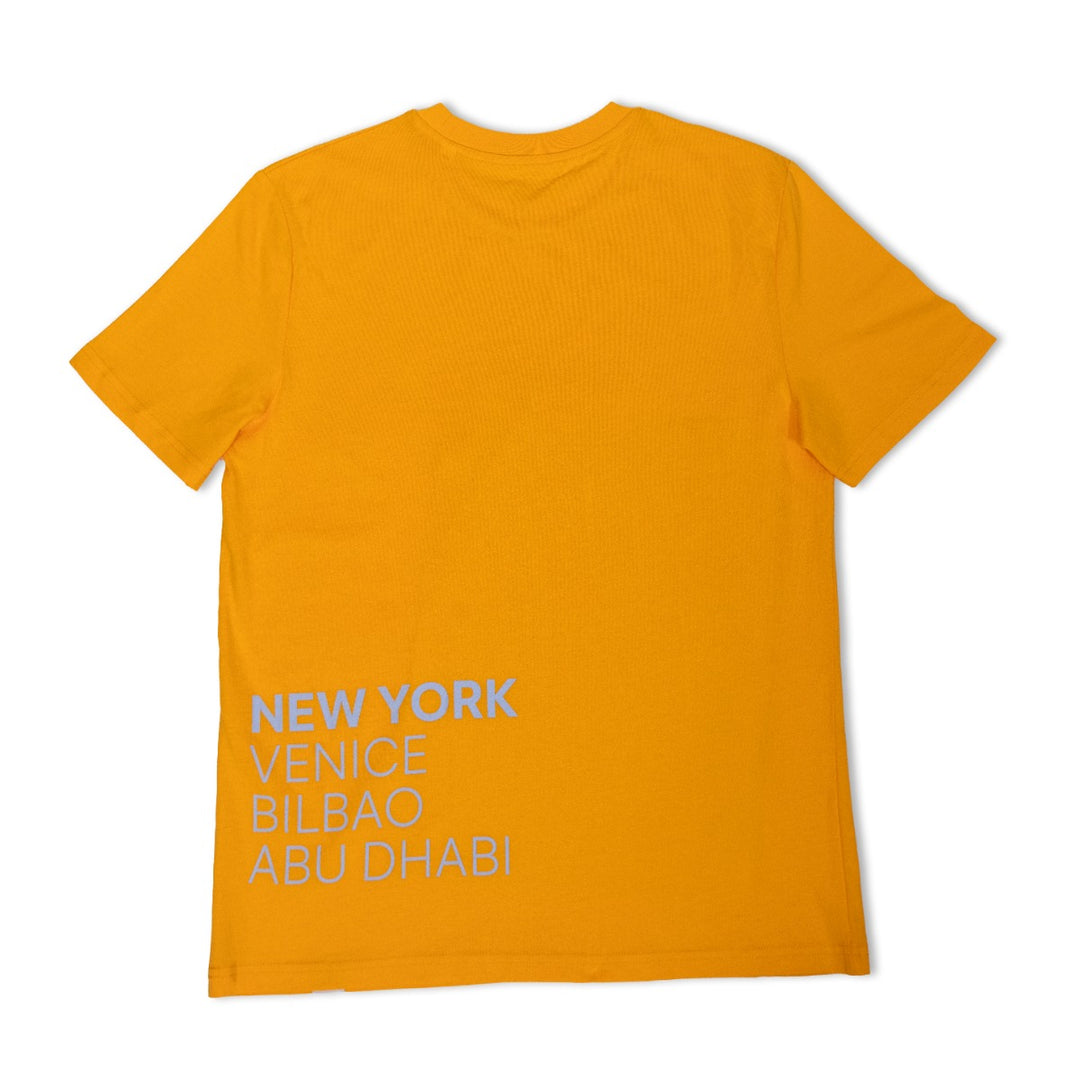 The Guggenheim Constellation T-Shirt, New York Yellow, is an art-inspired organic cotton crewneck featuring bold white text—NEW YORK, VENICE, BILBAO, ABU DHABI—on the lower back. The shirt is shown flat with its back side visible.