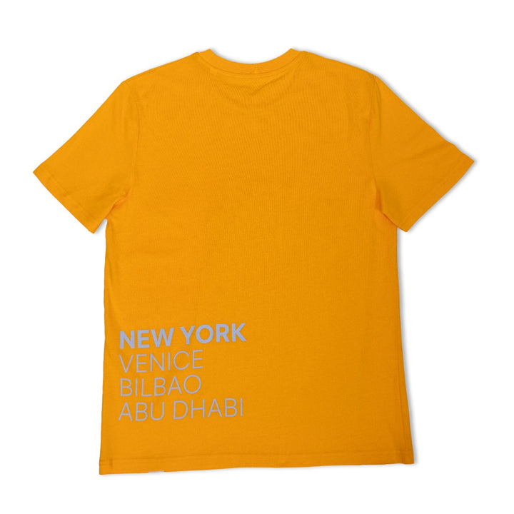 The Guggenheim Constellation T-Shirt, New York Yellow, is an art-inspired organic cotton crewneck featuring bold white text—NEW YORK, VENICE, BILBAO, ABU DHABI—on the lower back. The shirt is shown flat with its back side visible.